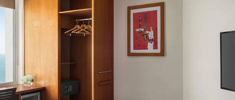 Habitación de hotel con un armario de madera, un escritorio con computadora, un banco acolchado verde, una obra de arte enmarcada en la pared y una ventana con vistas.