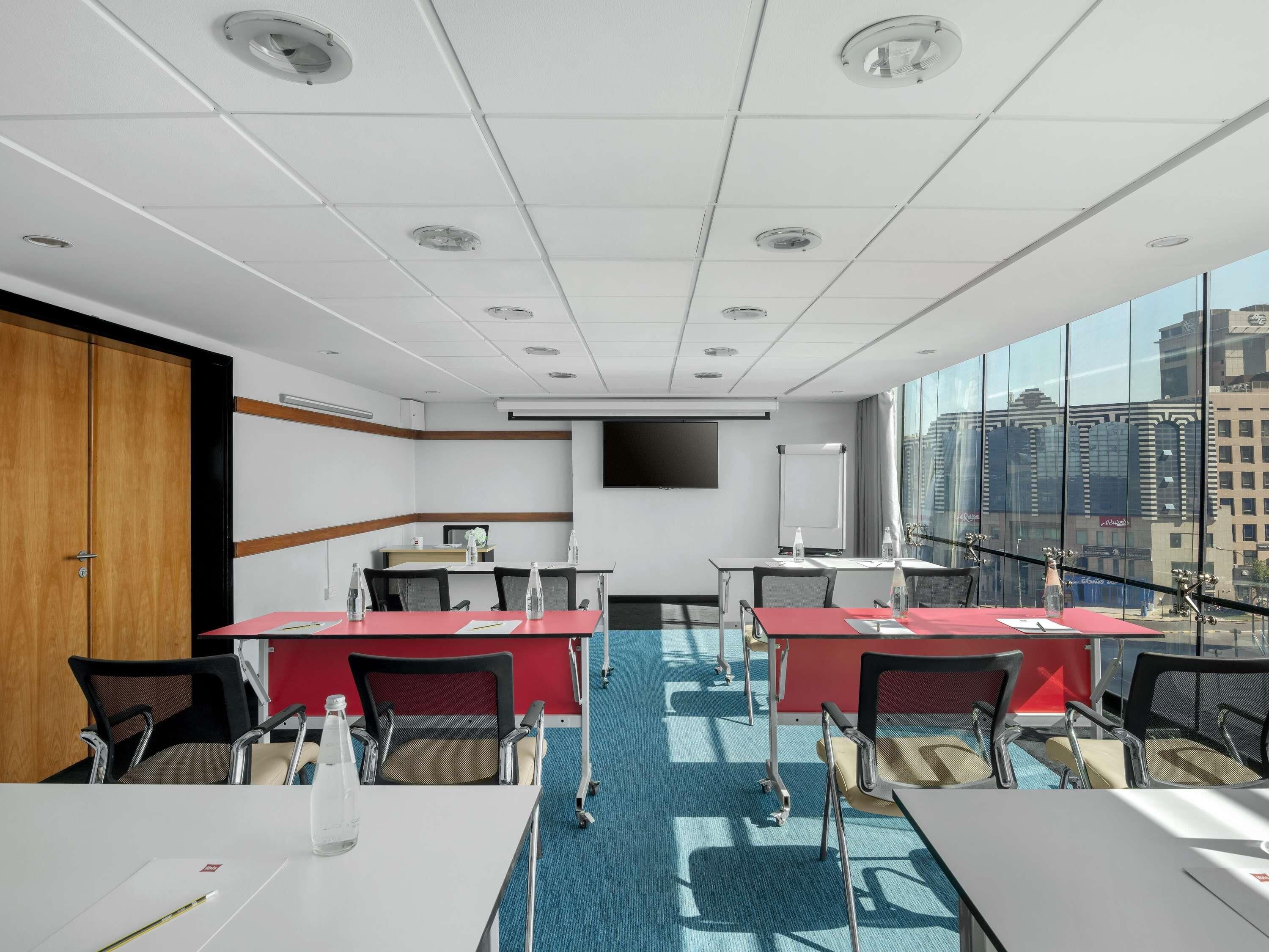 A conference room with tables, chairs, a projector screen, and a large window with a city view.