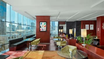 Un moderno vestíbulo de hotel con pared de vidrio, zonas de estar, un mostrador de recepción y vistas a la ciudad.