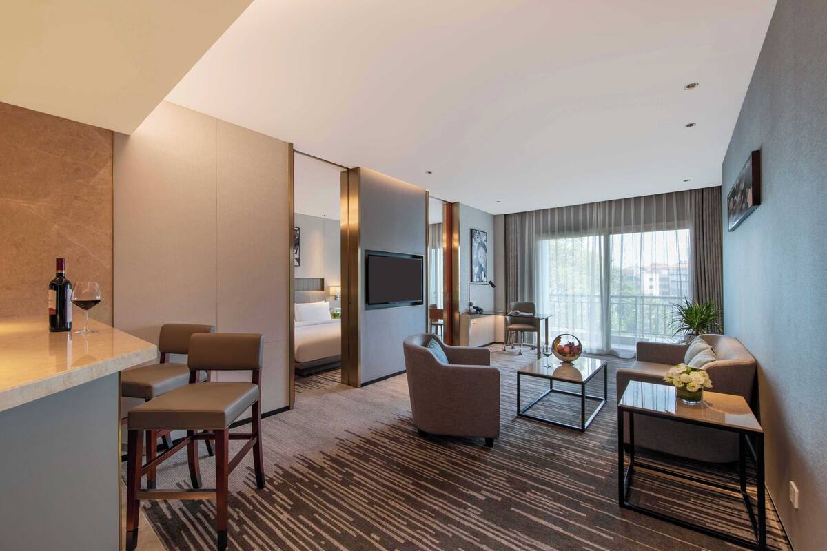 A modern hotel room with a living area, a dining area, and a bedroom.