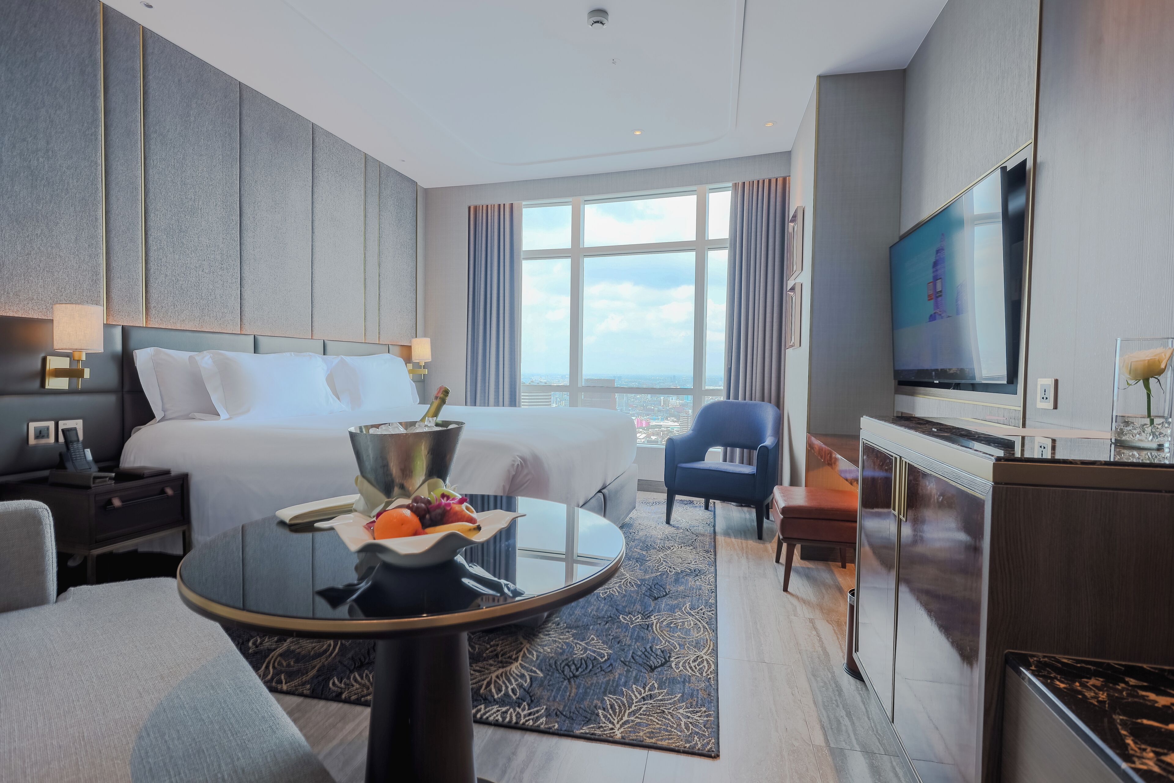 A modern hotel room with a large bed, a TV, a desk, and a view of the city.