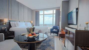 A modern hotel room with a large bed, a TV, a desk, and a view of the city.