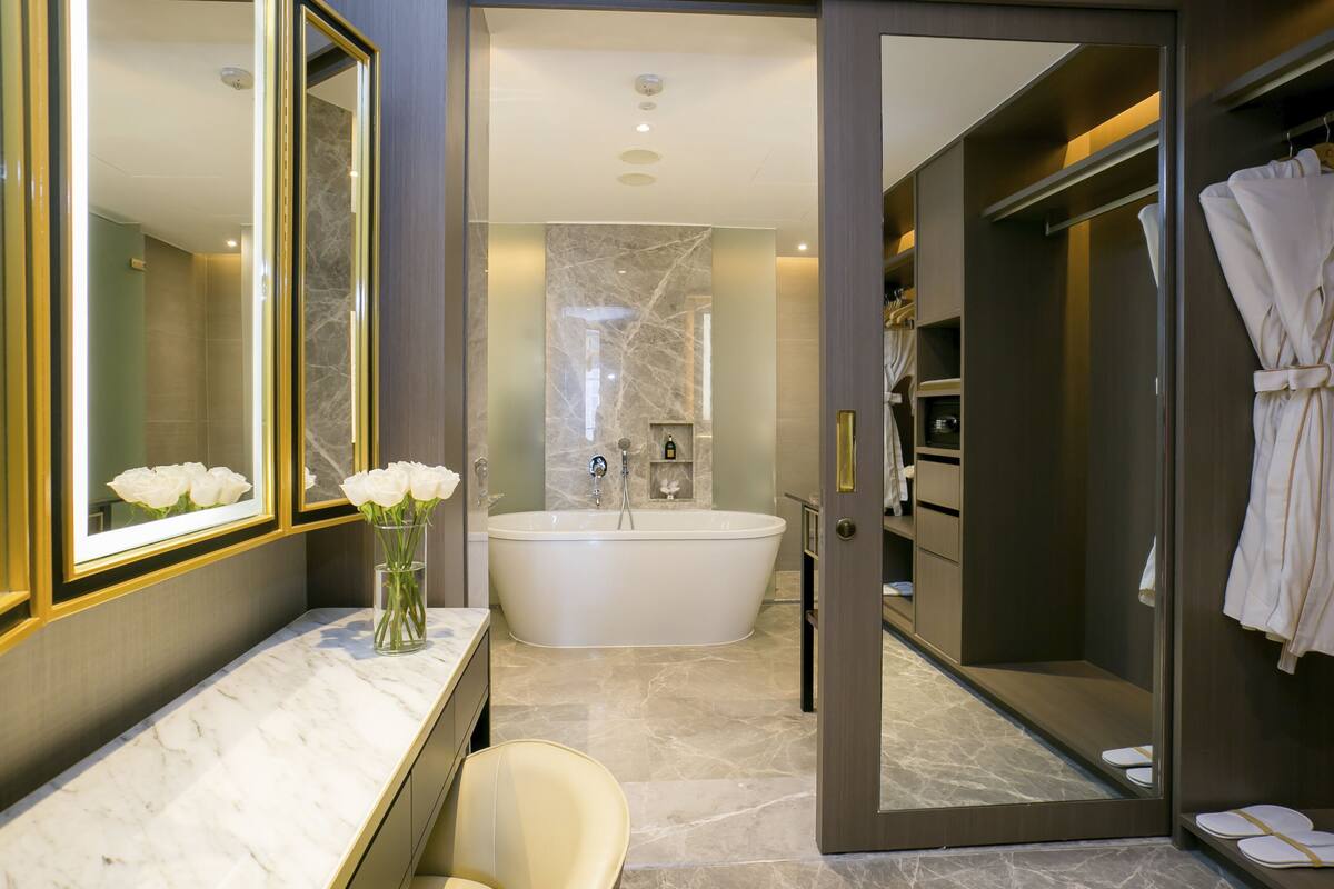 A modern bathroom with a large bathtub, a vanity with a marble countertop, and a mirror with a gold frame.