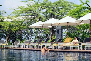 Un espace aménagé au bord de la piscine, avec des chaises longues et des parasols, entouré d’une végétation luxuriante.