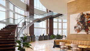 A spacious lobby with a modern staircase, seating area, and a large abstract painting on the wall.