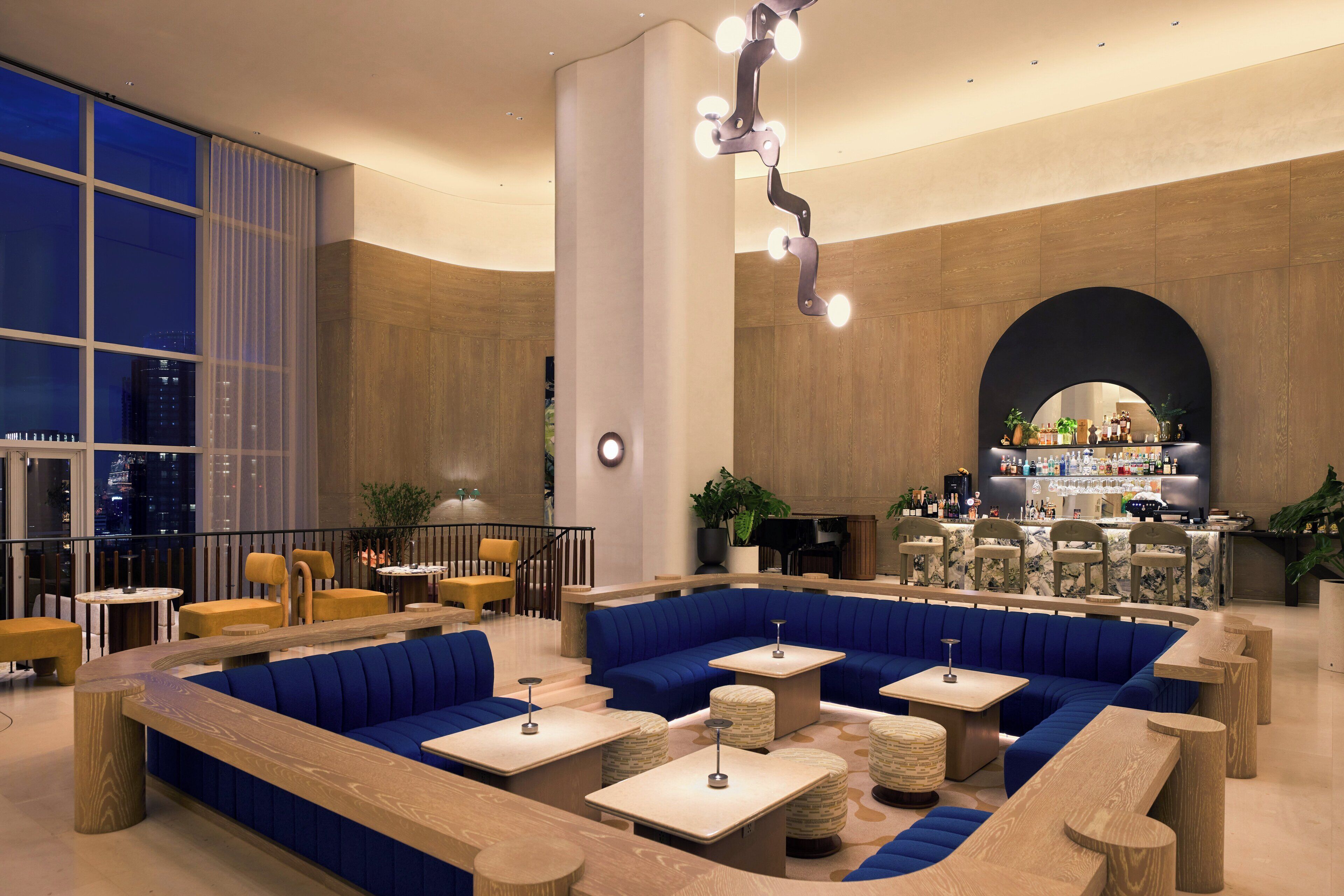 A modern lounge area with blue seating, wooden tables, and a bar in the background.