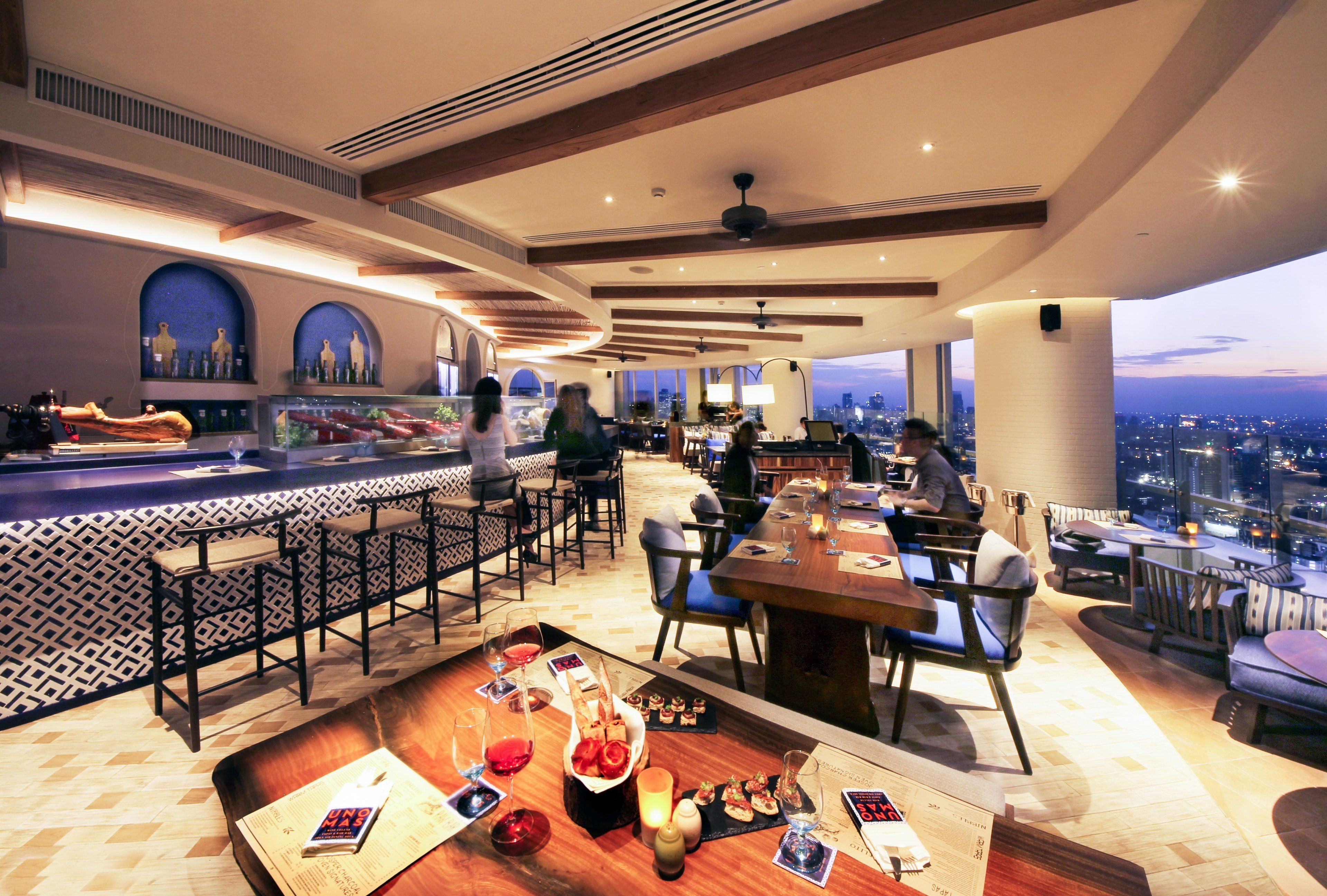 Un restaurante moderno con zona de bar, techos altos y vistas a la ciudad.