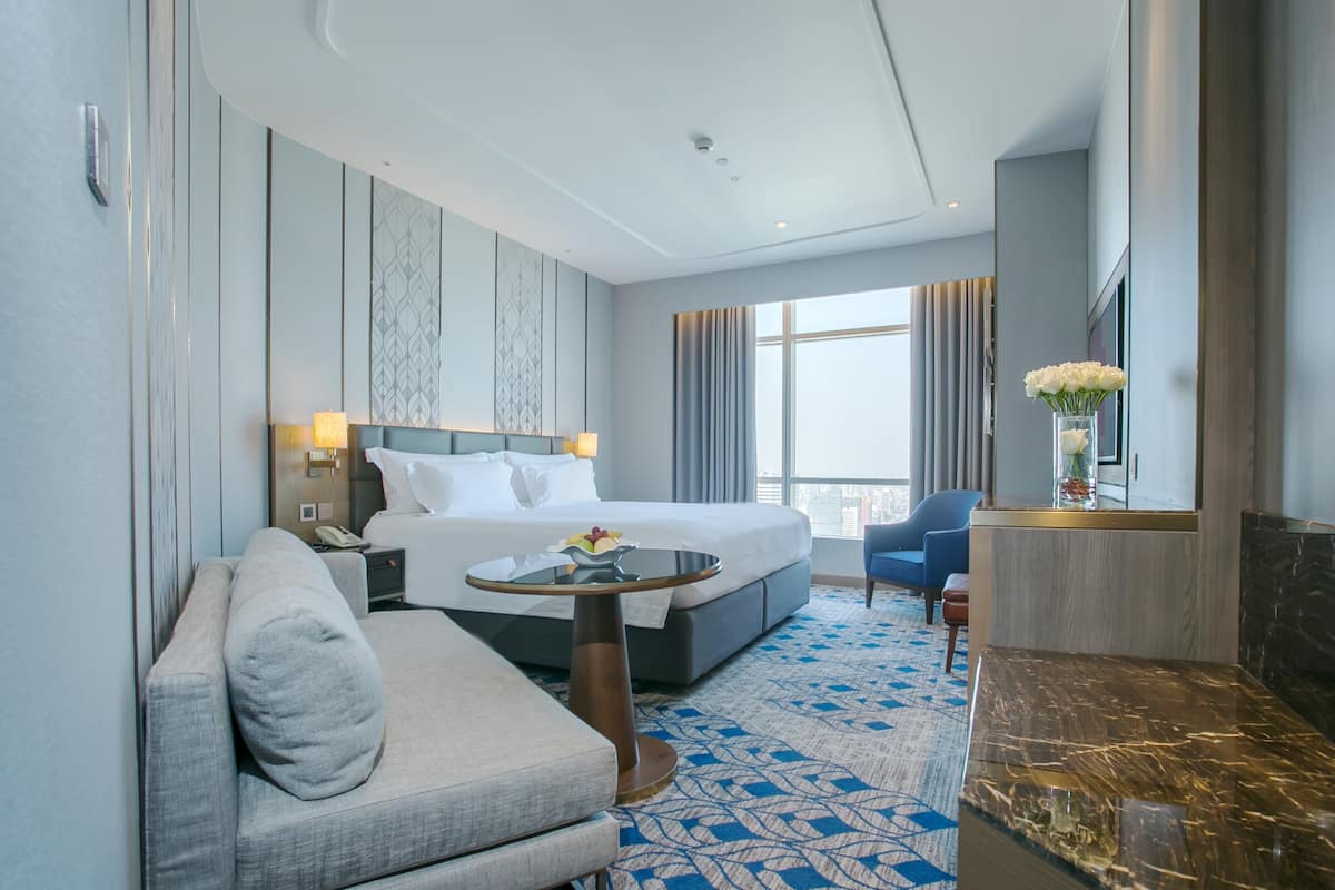 A hotel room with a bed, a sofa, a small table, a TV, and a view of the city.