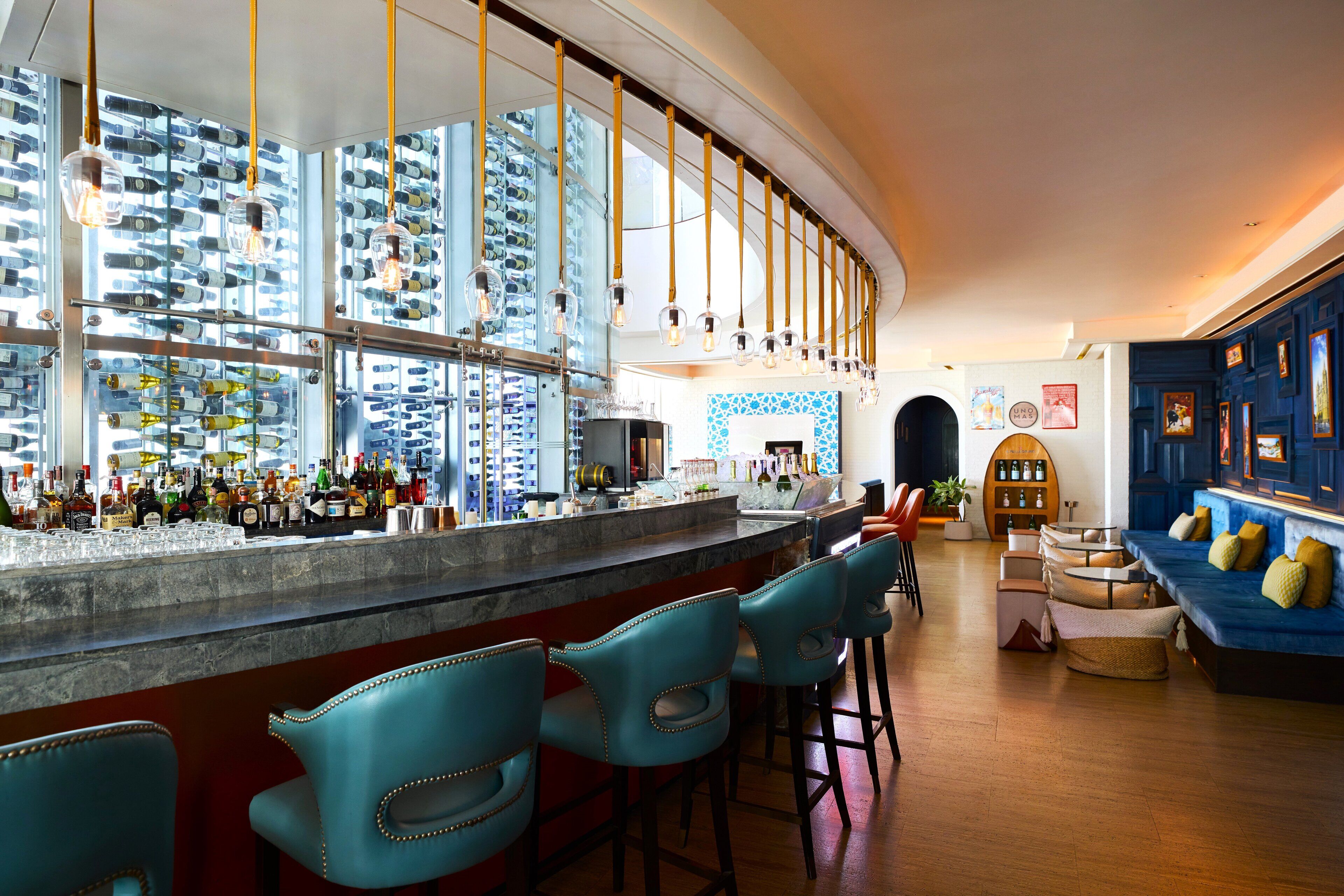 A bar area with a curved counter, blue bar stools, and a variety of bottles and glasses on shelves.