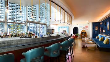 A bar area with a curved counter, blue bar stools, and a variety of bottles and glasses on shelves.