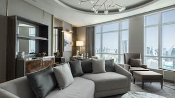 A modern hotel room with a sectional sofa, a dining area, a large window with a city view, and a chandelier.