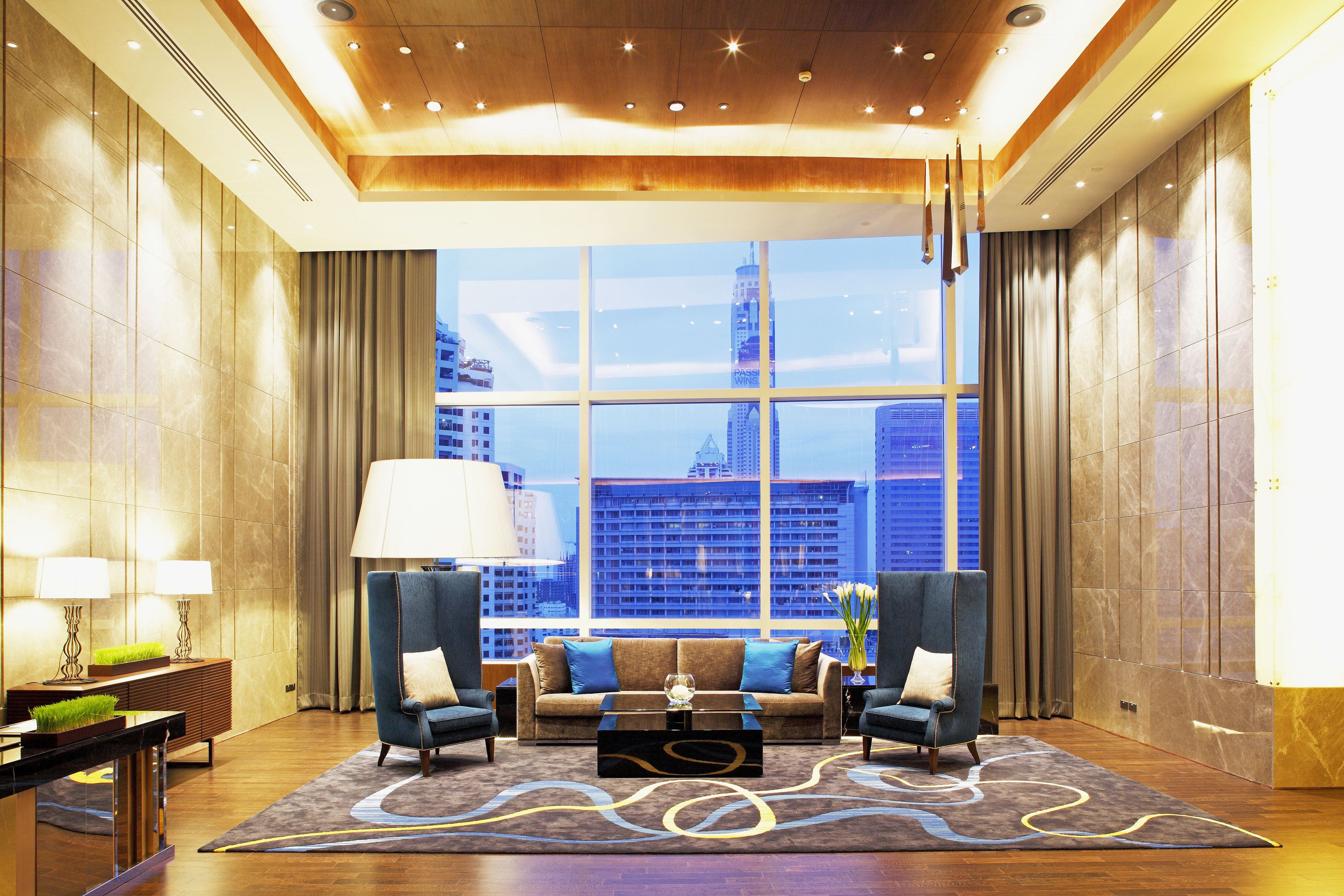 A spacious lobby with a large window offering a city view, a sofa set, two armchairs, and a coffee table.