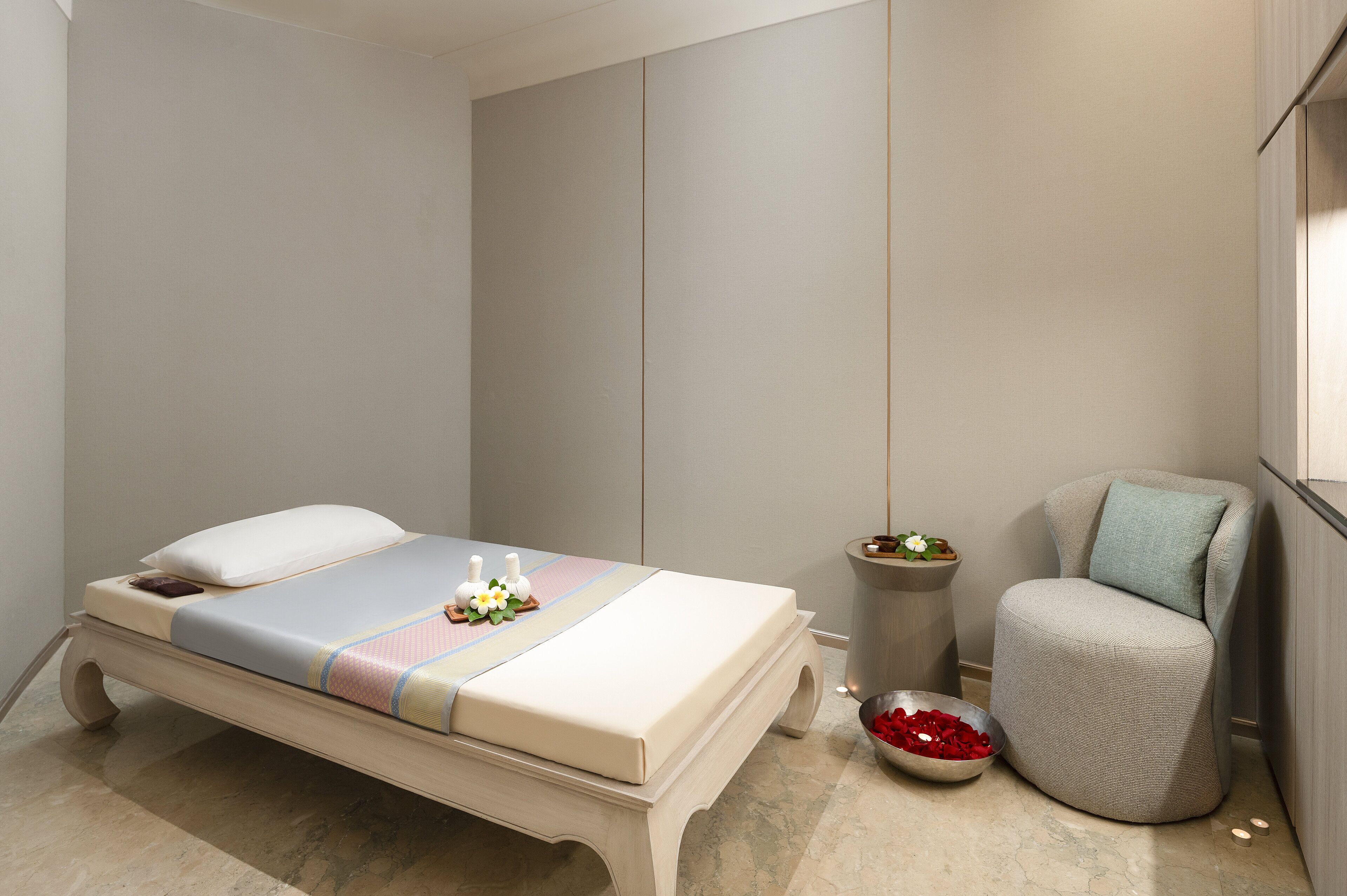 A neatly arranged bedroom with a bed, a small round table, a chair, and a bowl of red flowers.