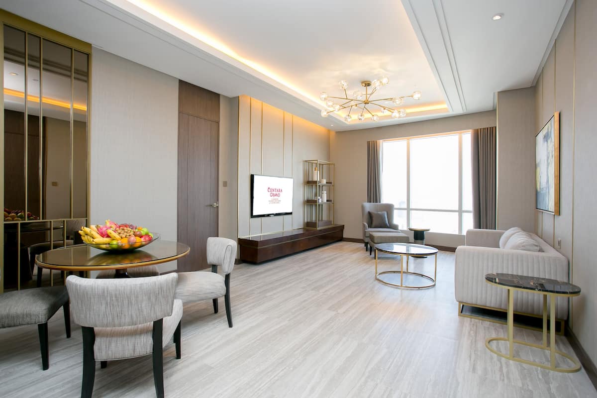 A modern hotel room with a dining area, a sofa, a TV, and a large window.