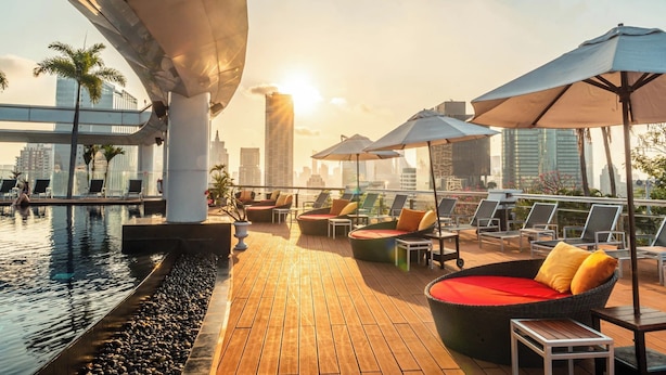 A rooftop pool area with lounge chairs and umbrellas, overlooking a cityscape.