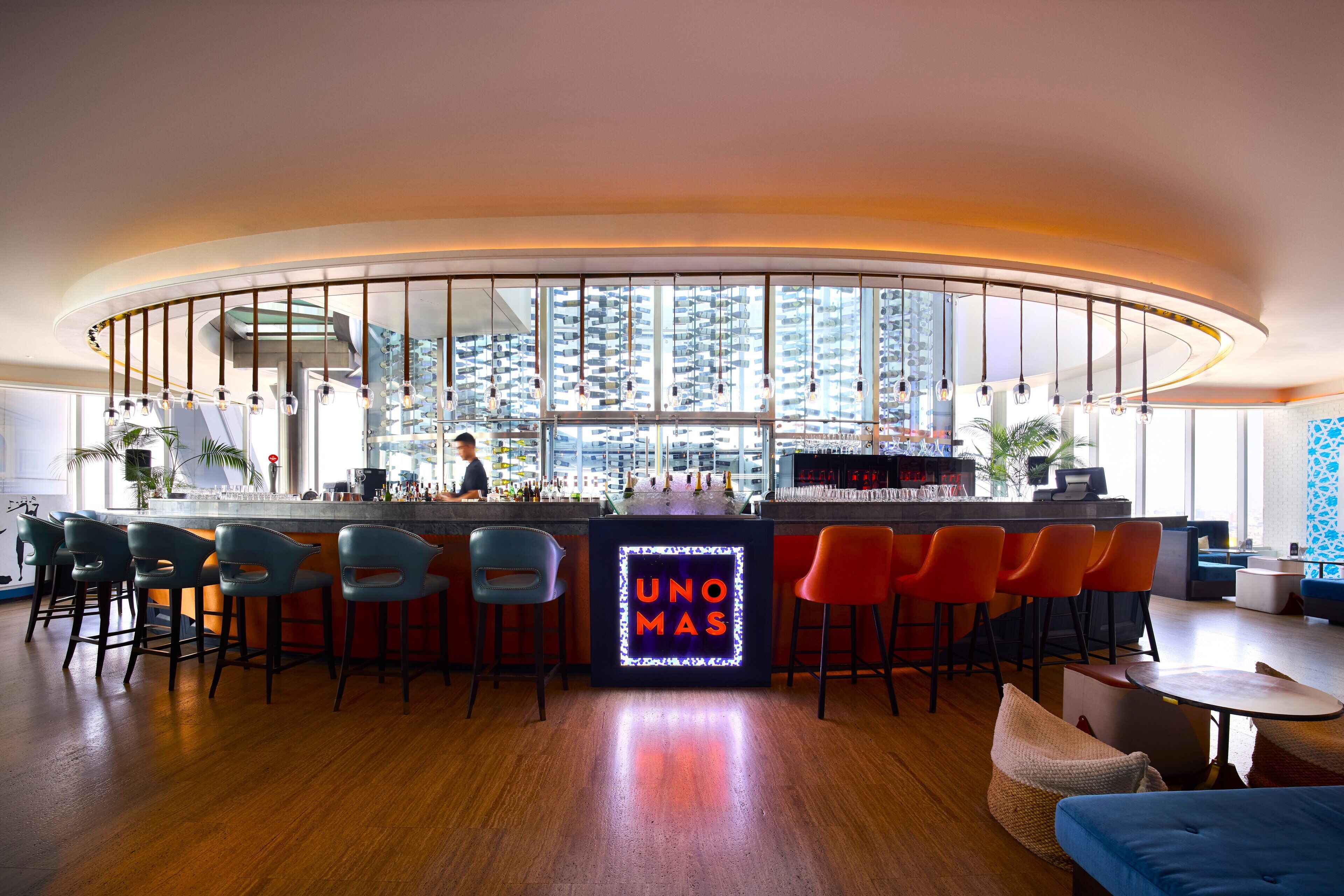 A modern bar area with a neon sign, bar stools, and a view of high-rise buildings.