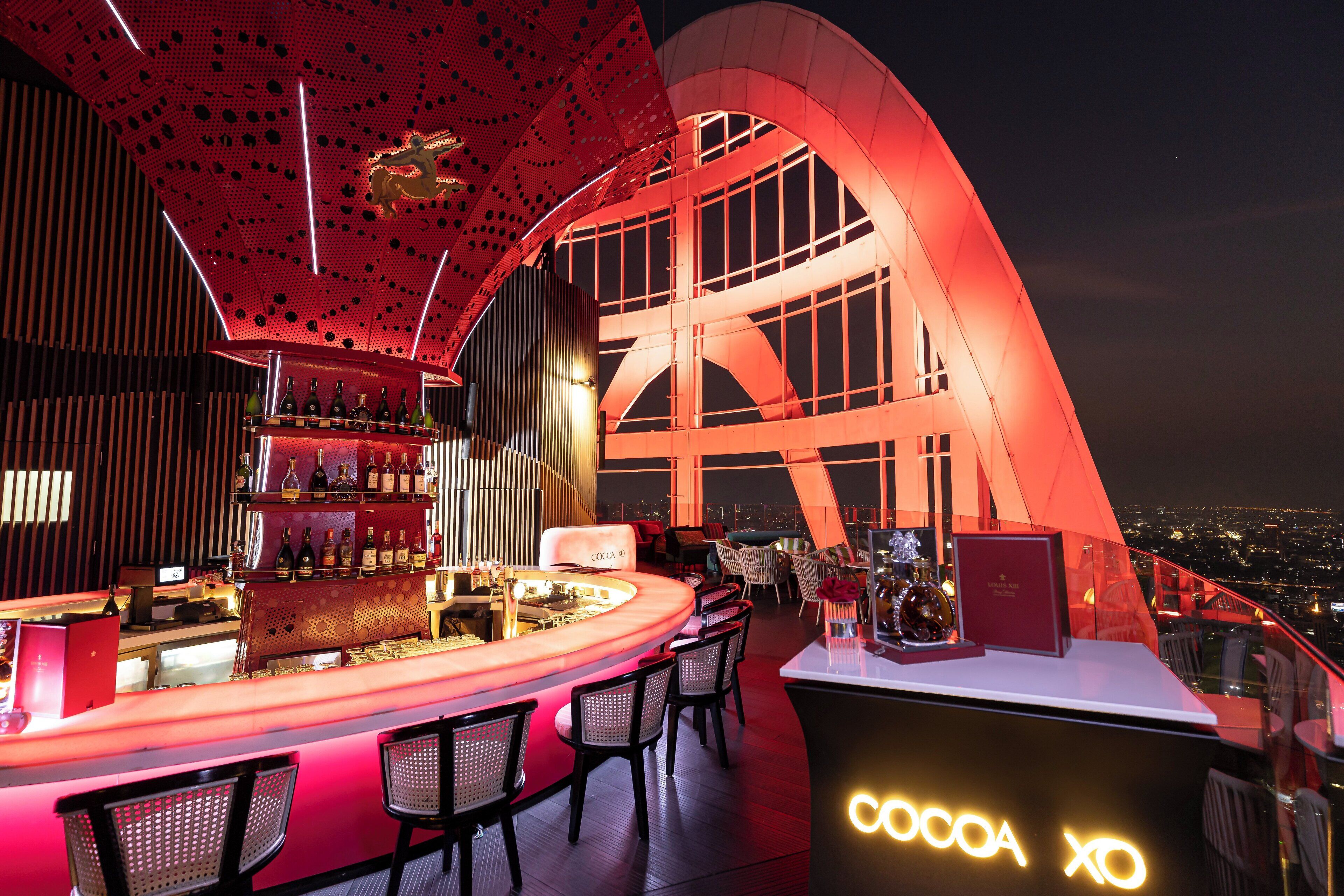 A modern bar with a curved counter, seating, and a view of the city at night.