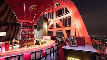 A modern bar with a curved counter, seating, and a view of the city at night.