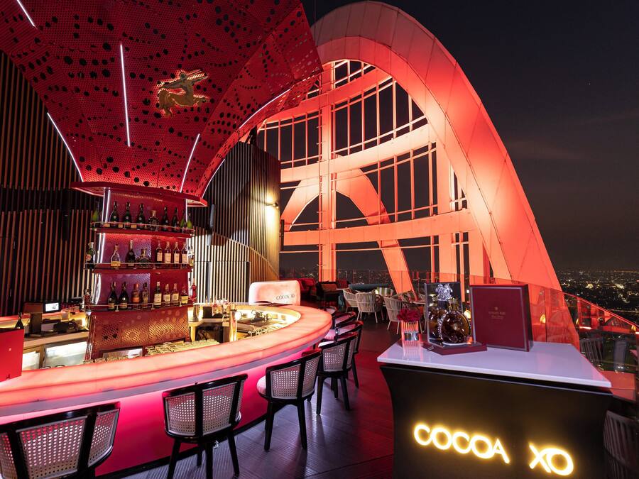 A modern bar with a curved counter, seating, and a view of the city at night.