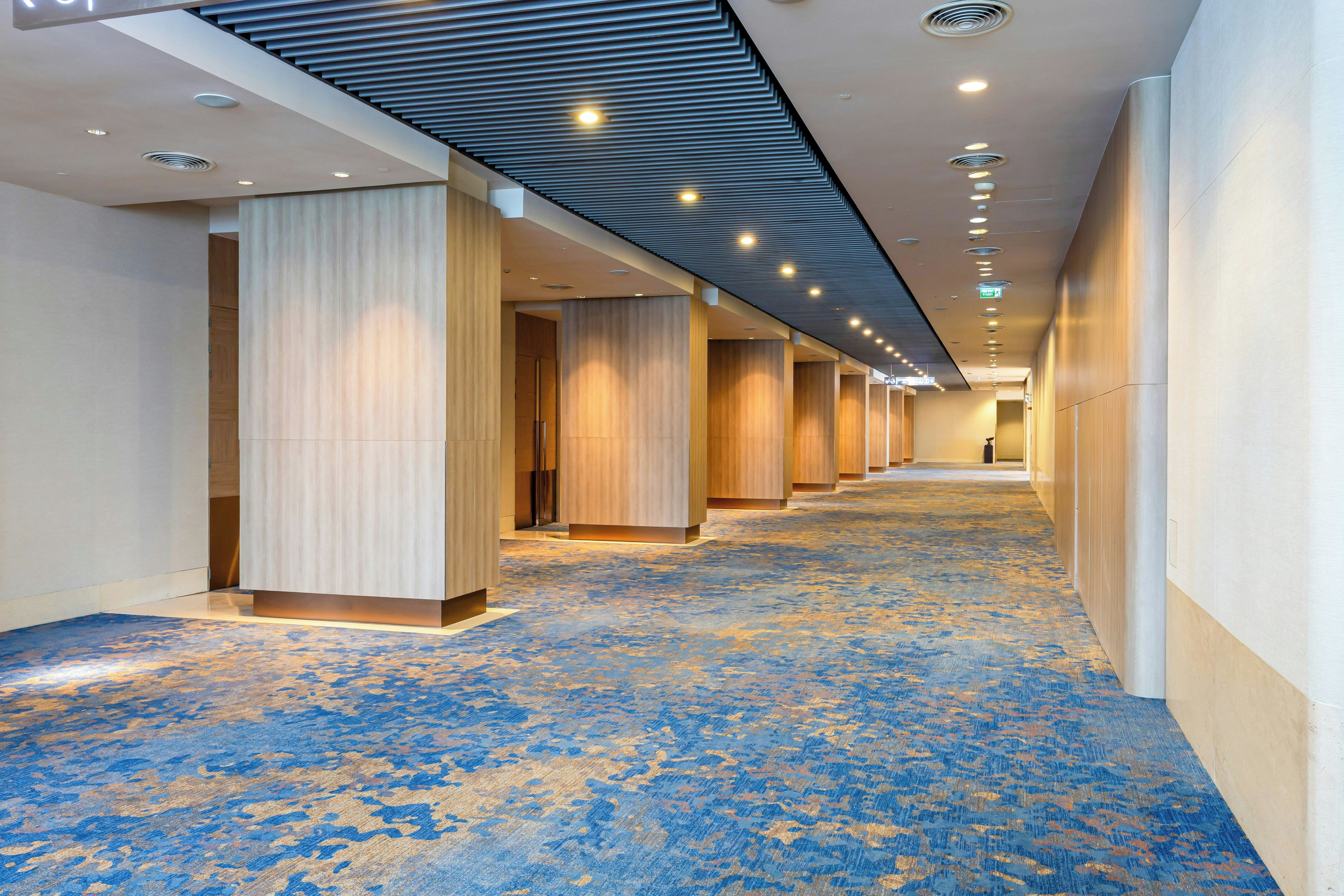 Een hotelgang met een kamerjas patroon, houten paneelwanden en inbouwverlichting.