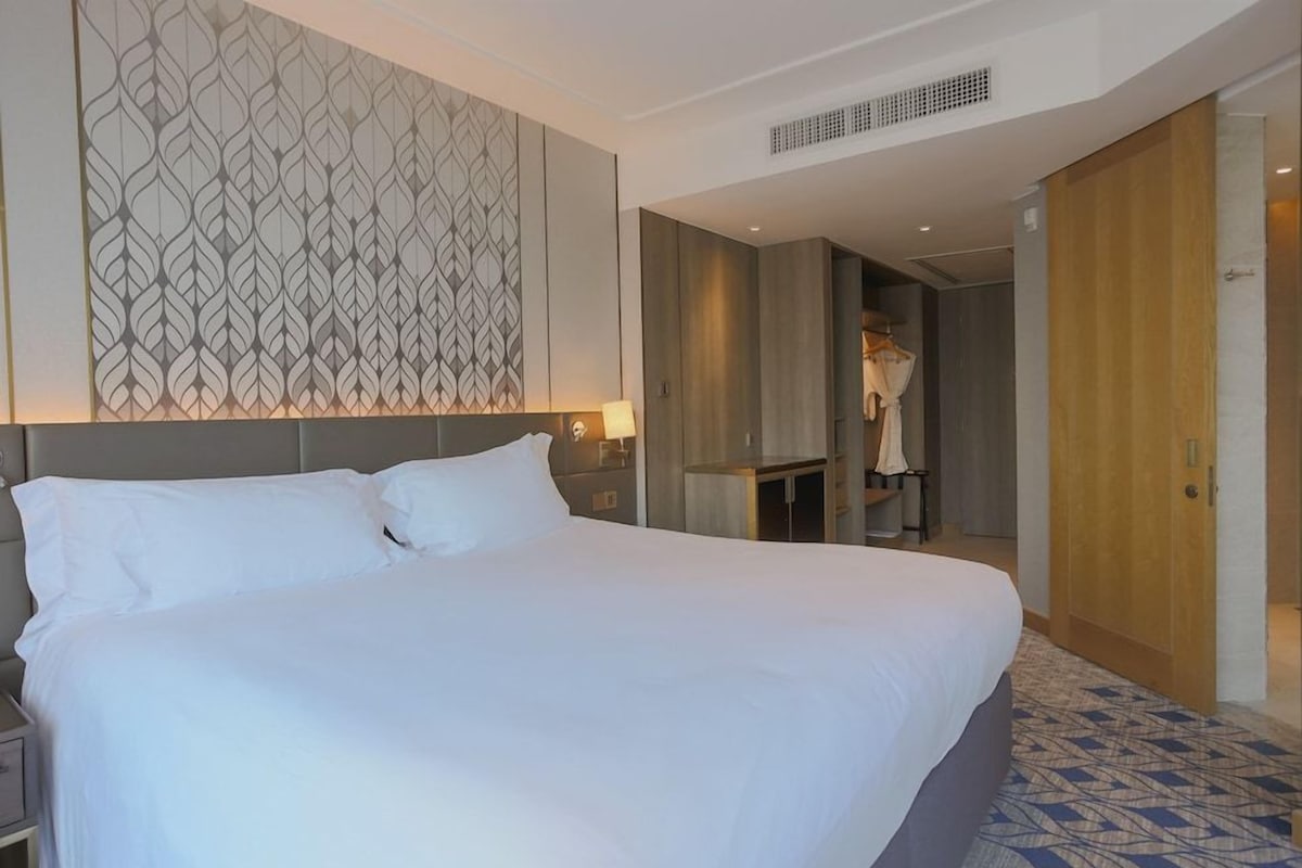 A hotel room with a large bed, a patterned wall, a wardrobe, and a mirror.