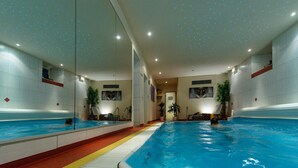 An indoor swimming pool with mirrored walls, a central walkway, and potted plants. - AKZENT Hotel Goldner Stern (Wiesenttal)