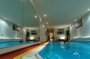 Piscina interior com paredes espelhadas, um caminho central e plantas em vasos.