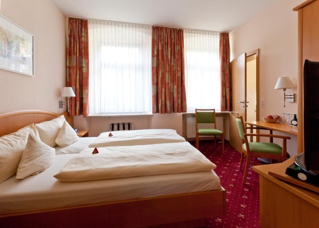 A hotel room with two beds, a desk, a chair, a television, and a window with curtains.