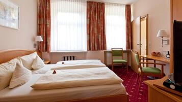 A hotel room with two beds, a desk, a chair, a television, and a window with curtains.