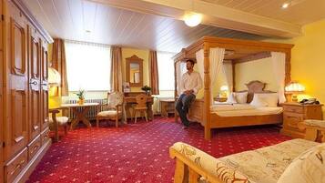 A traditional room with a four-poster bed, a desk with a chair, a radiator, and a red carpet.