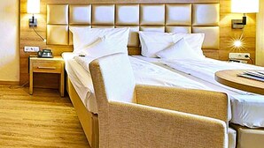A hotel room with a wooden ceiling, a large bed with white linens, two bedside tables, and a chair. - AKZENT Hotel Goldner Stern (Wiesenttal)