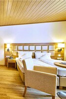 Quarto de hotel com teto de madeira, uma cama grande com roupa de cama branca, duas mesas de cabeceira e uma cadeira.
