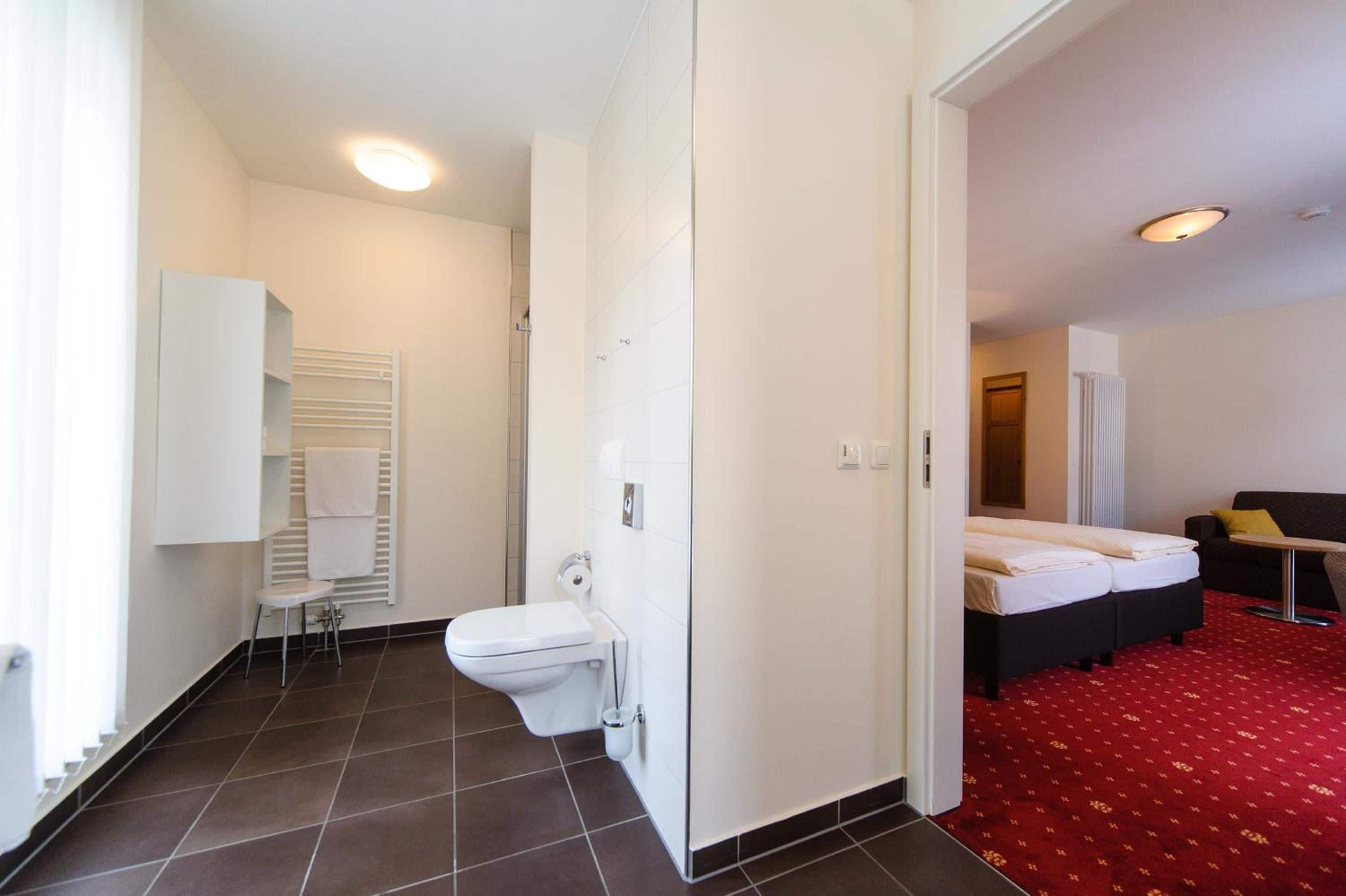 Ett hotellrum med en toalett, ett litet sängbord, en säng och ett område med rött heltäckningsmatta.