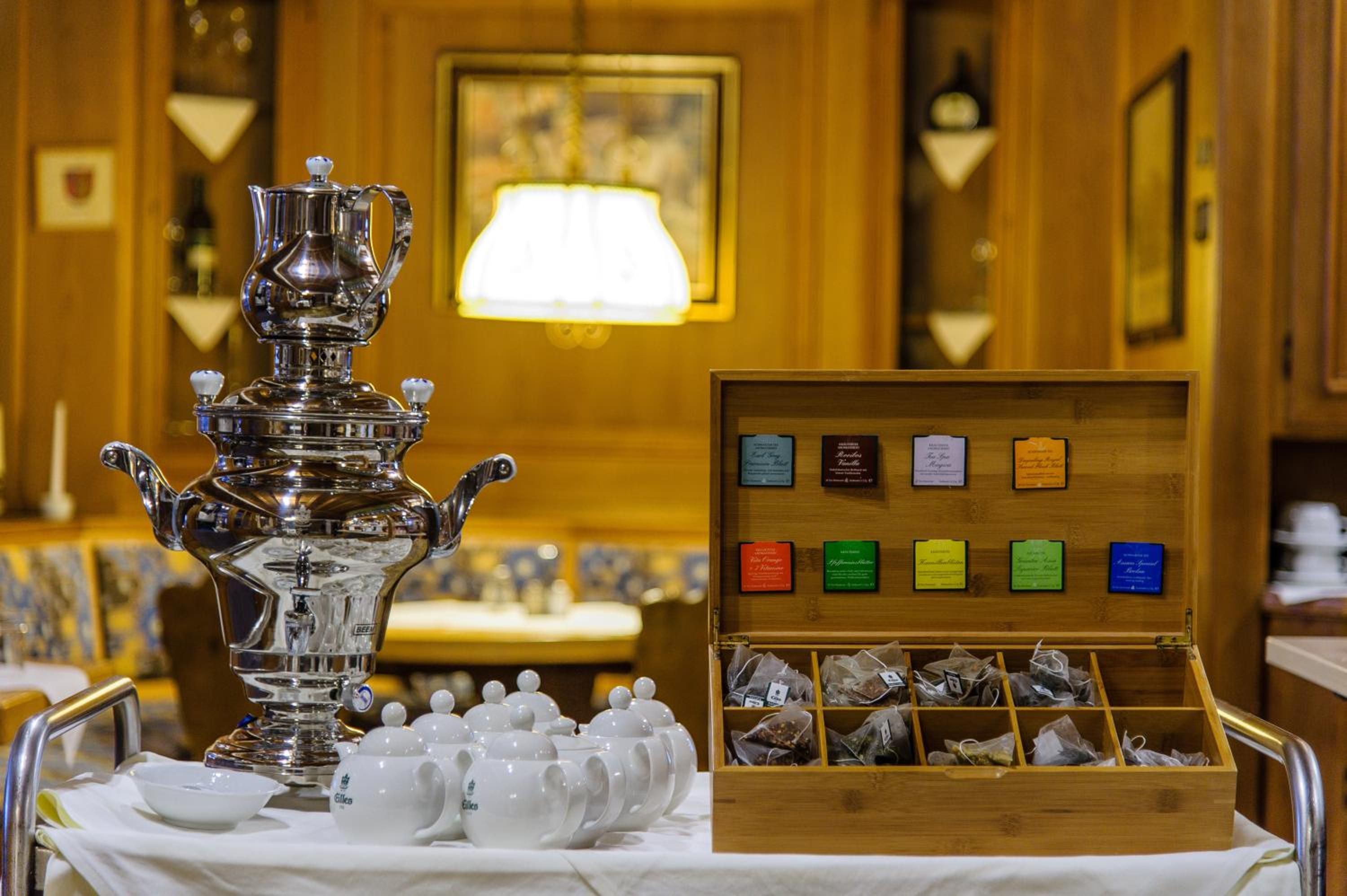 A tea service set with a silver teapot and cups, a wooden box with tea bags, and a table with a white tablecloth.