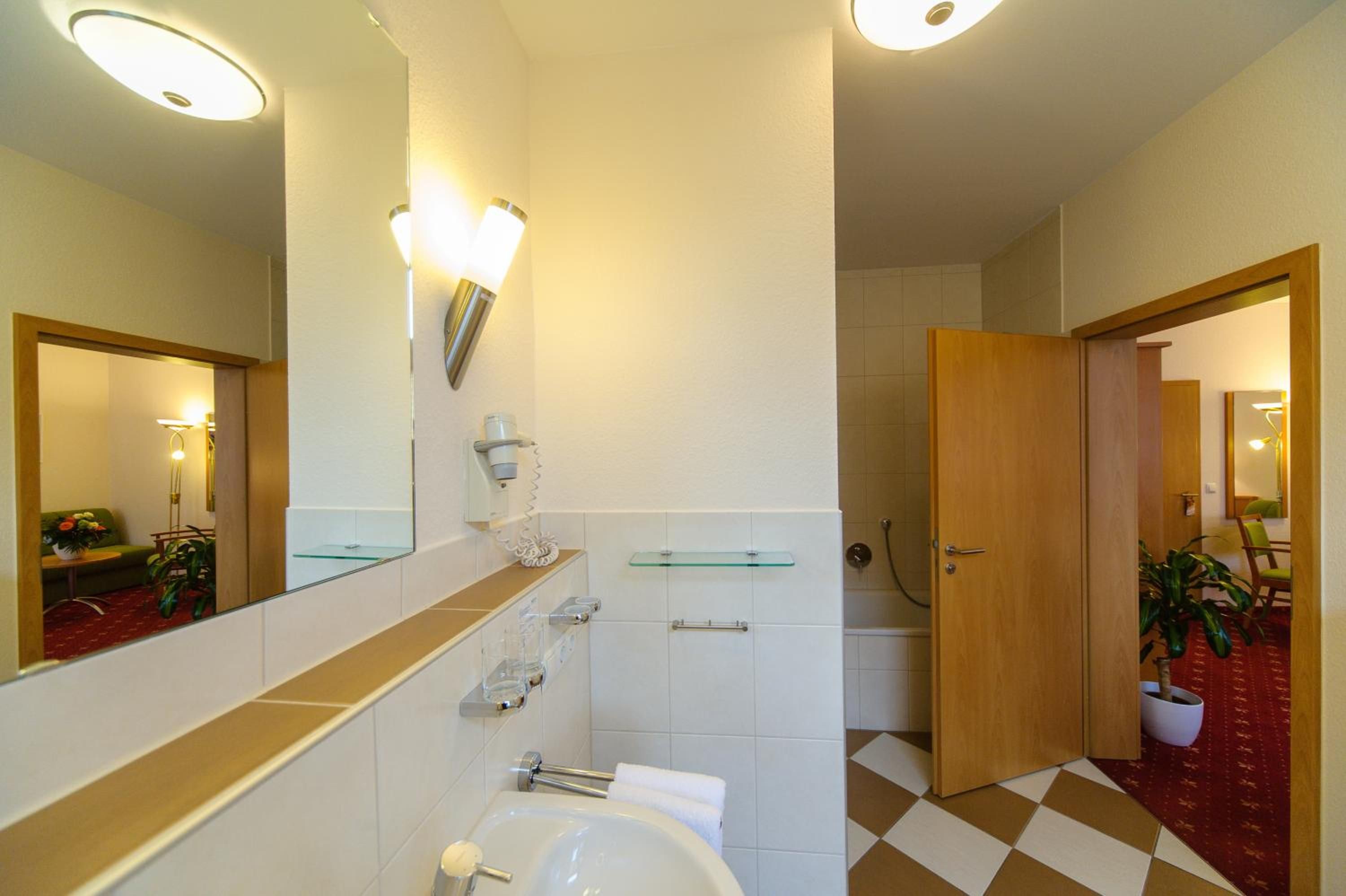 A bathroom with a white sink, mirror, and glass shelves. There is a shower area visible in the background.