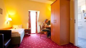 Una camera d'albergo con un letto, una scrivania, una sedia, un armadio e una porta che dà su un bagno.