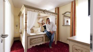 A four-poster bed with a canopy, a mirror, and a red patterned carpet in a room with cream walls and a door.