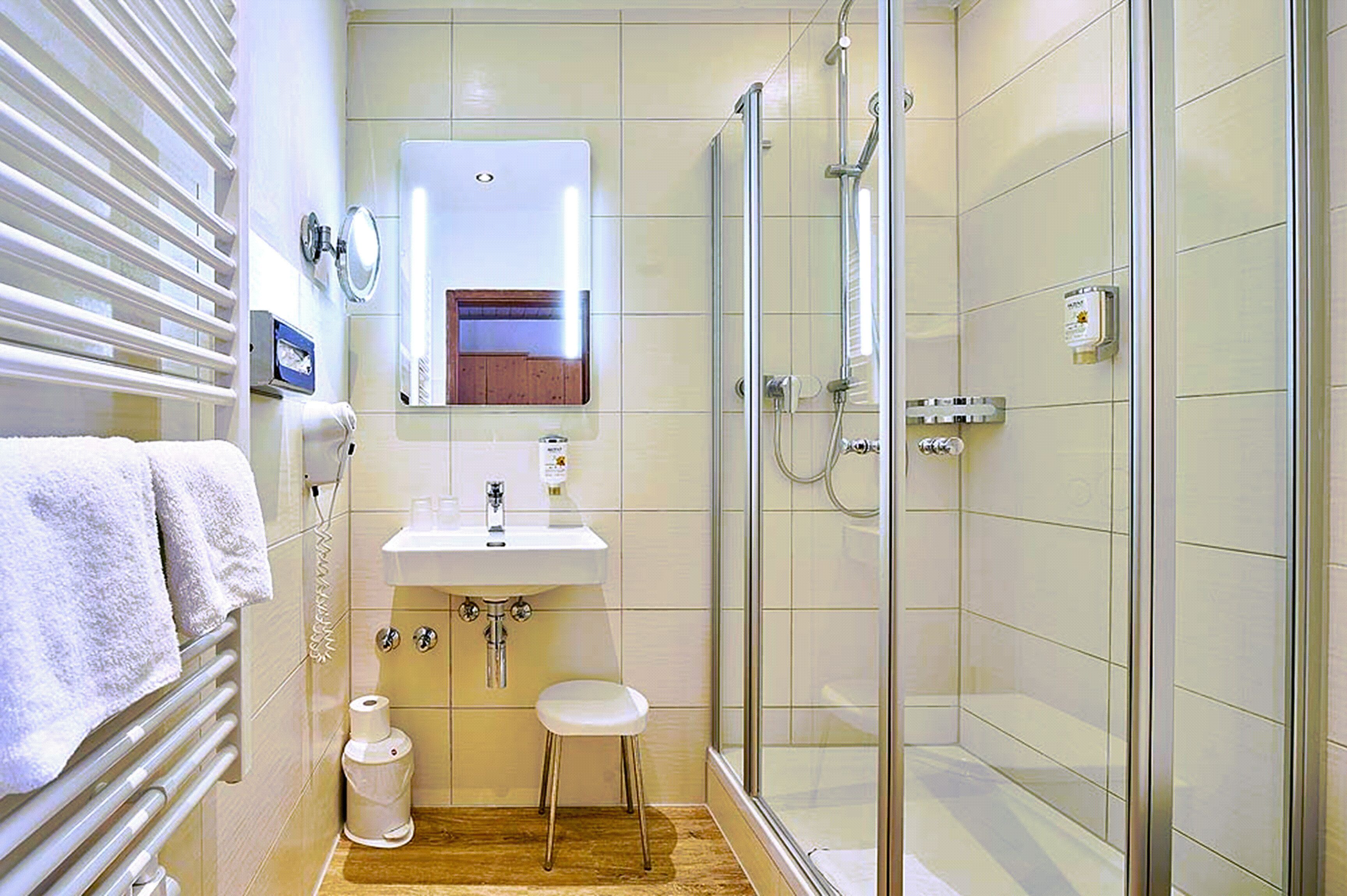 Een moderne badkamer met een douchecabine van glas, een witte wastafel en een klein krukje.