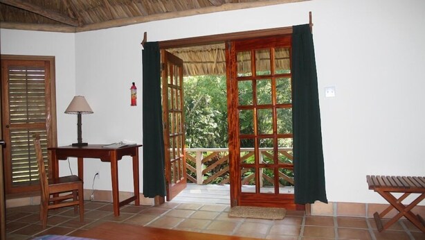 A room with a wooden door leading to a balcony, a small table with a lamp, and a bench. - The Lodge At Big Falls (Punta Gorda)
