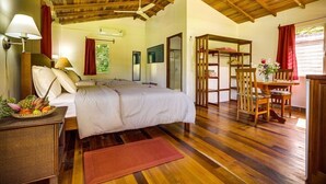 A bedroom with a wooden ceiling, a bed with white linens, a bedside table with a lamp, a fruit basket, and a wooden floor. - The Lodge At Big Falls (Punta Gorda)