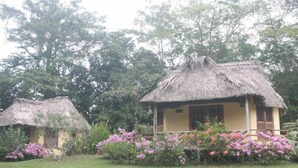 Two thatched-roof cottages with wooden shutters, surrounded by lush greenery and flowering plants. - The Lodge At Big Falls (Punta Gorda)