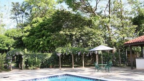 A swimming pool with a tiled edge, surrounded by a wooden deck and a garden with trees and a pergola. - The Lodge At Big Falls (Punta Gorda)