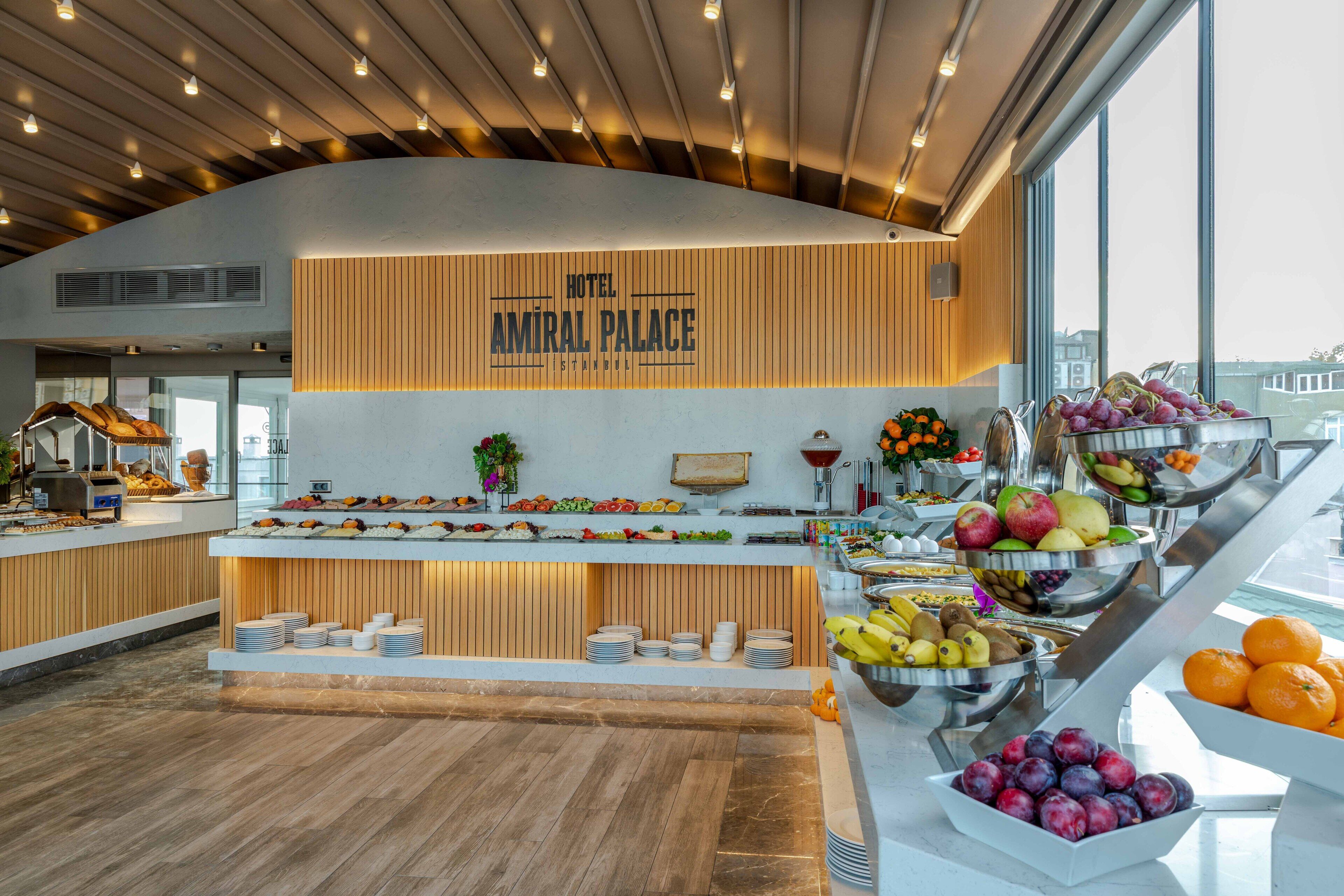 Ein Hotelbuffet mit einer Auswahl an Früchten und Gemüse, ein Schild mit der Aufschrift 'Hotel Amiral Palace' und ein modernes Interieur.