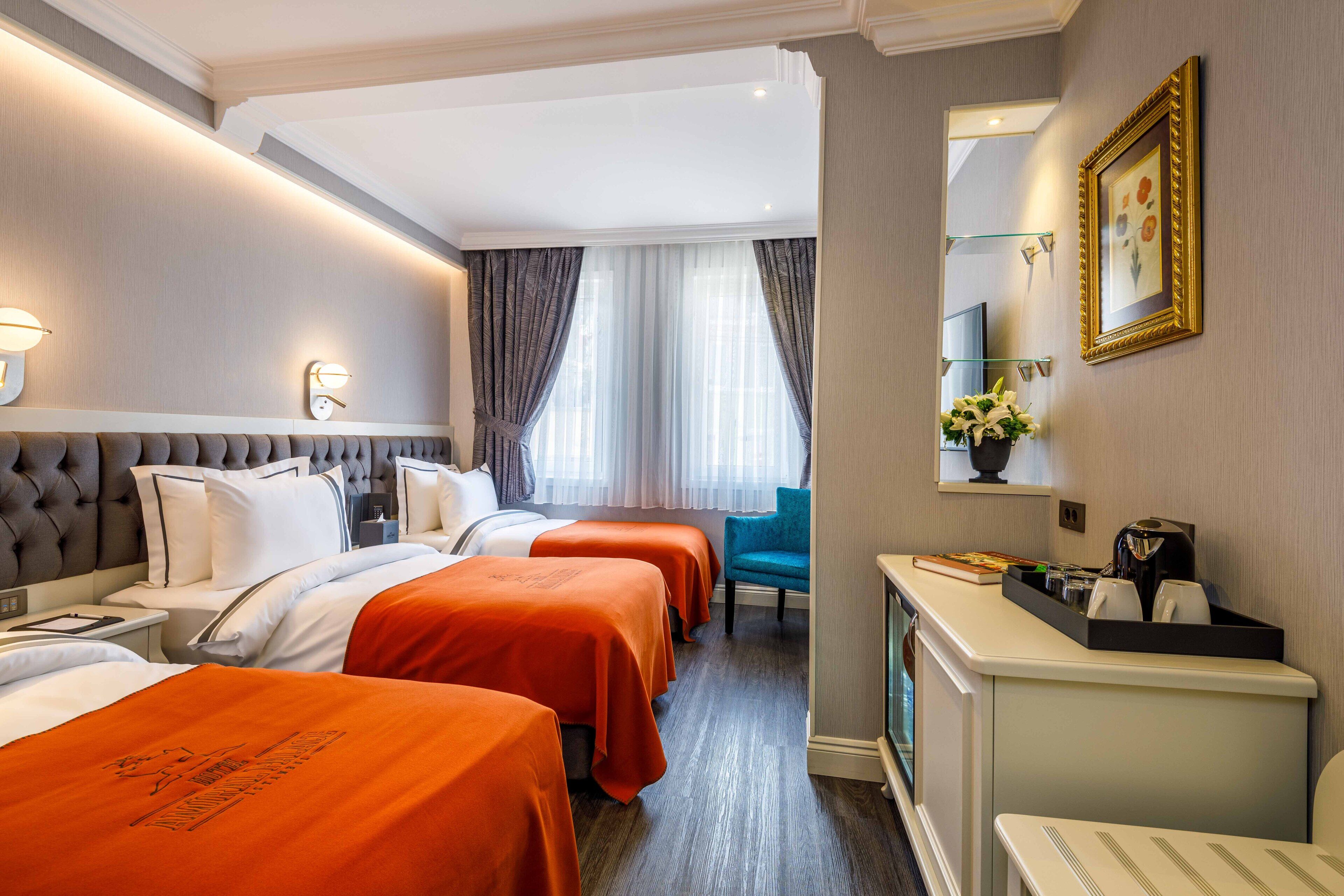 A hotel room with two beds, a desk, a chair, and a small kitchenette.