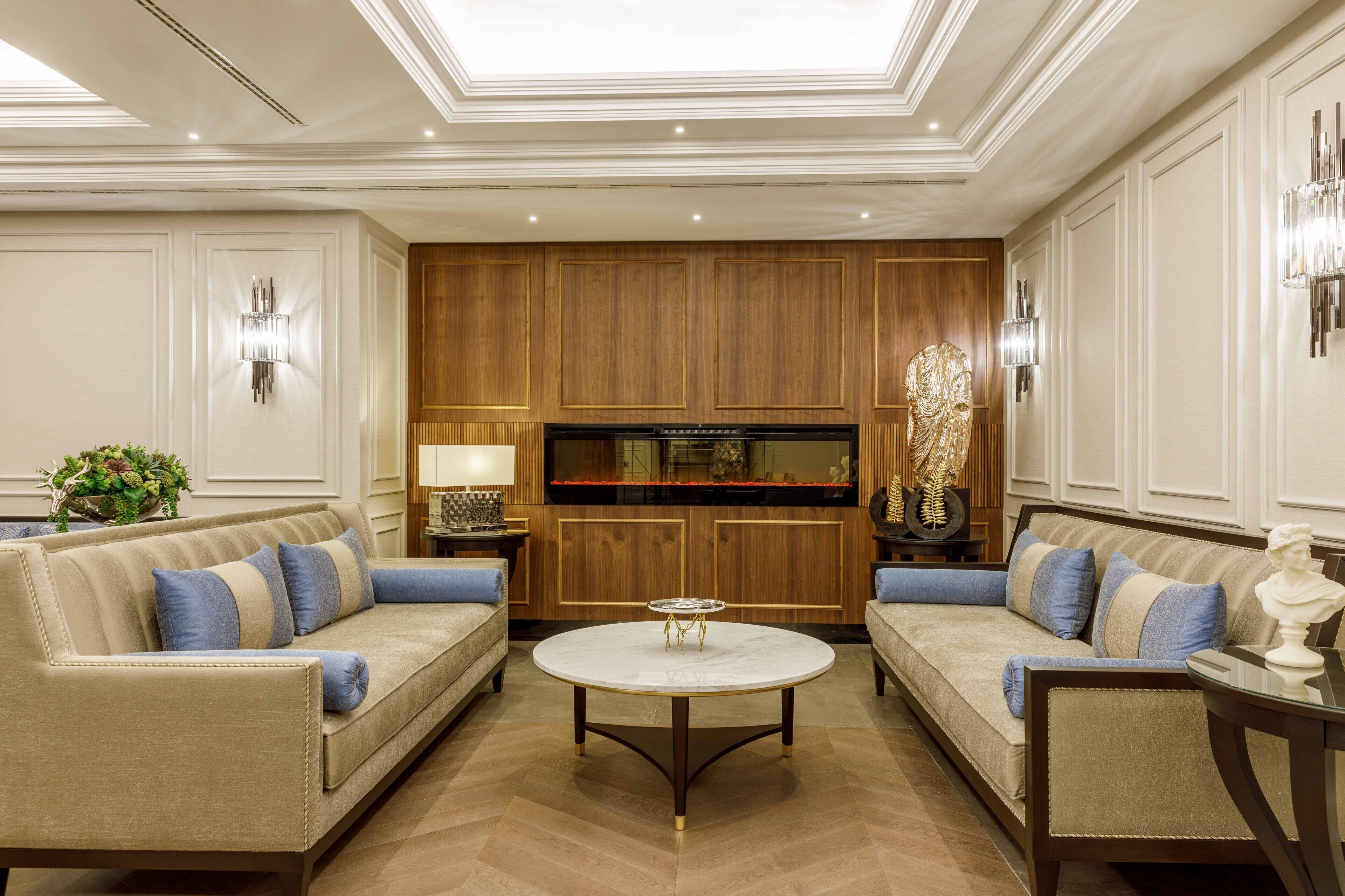 A luxurious living room with two sofas, a coffee table, wooden paneling, and wall sconces.