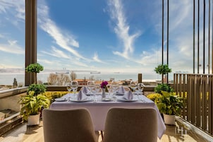 A dining table set for two with a view of a body of water and distant cityscape.
