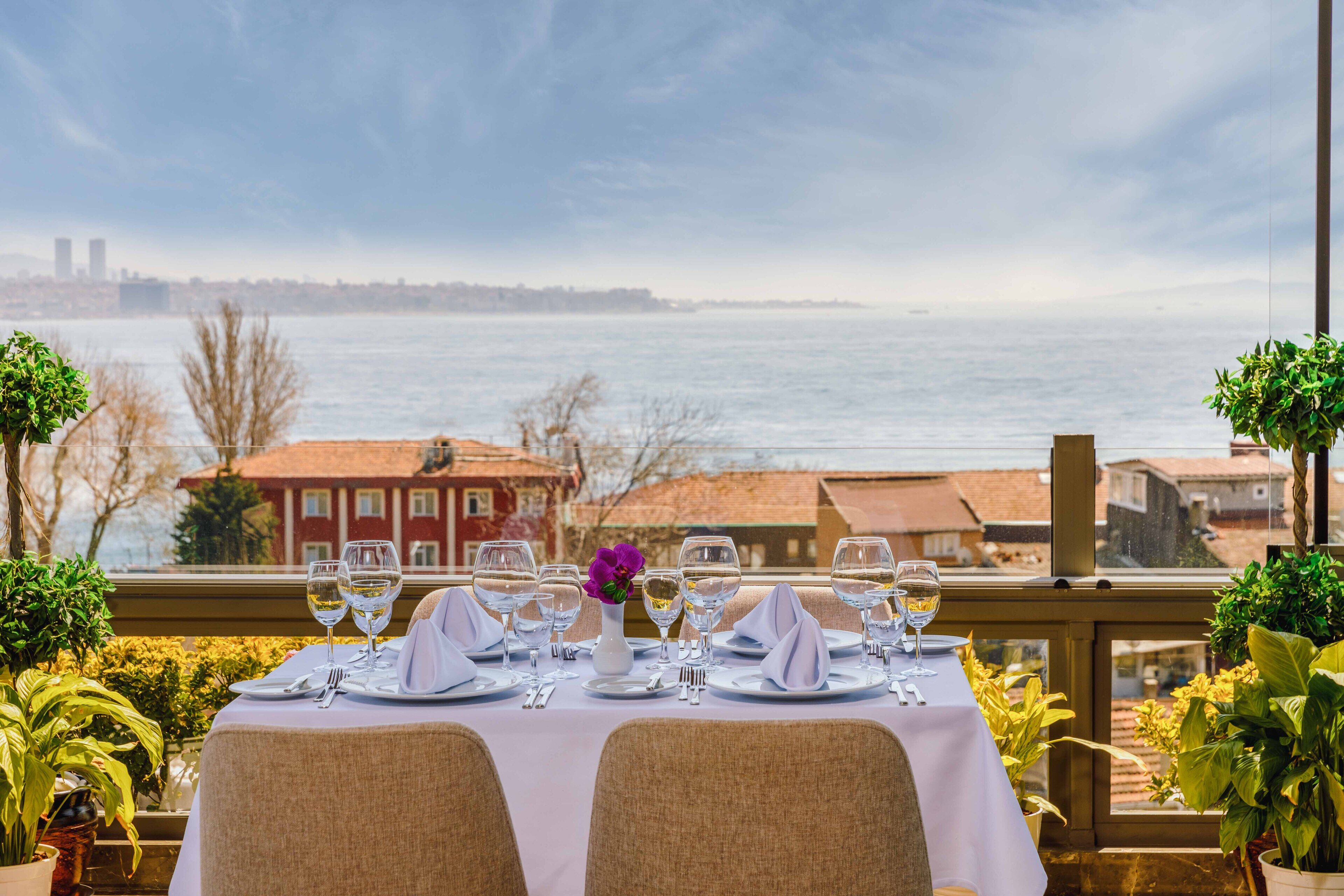 Mesa posta para refeição com vista para o mar e edifícios ao fundo.