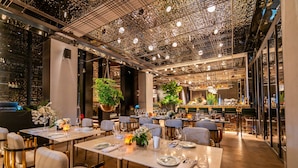 Ein Restaurant mit gedeckten Tischen, einer Bar und großen Kübelpflanzen.