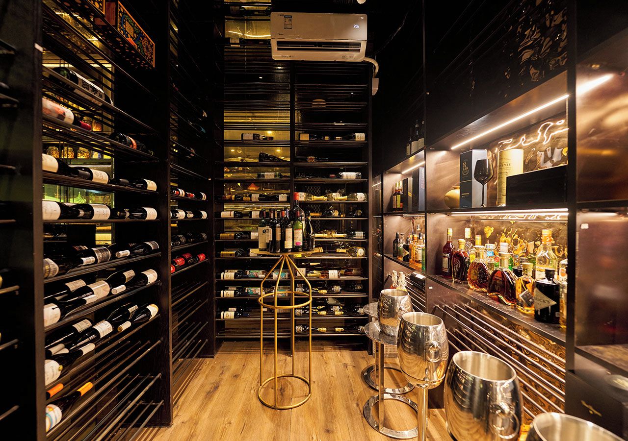 A wine cellar with shelves of wine bottles, a bar area with bottles and glasses, and a gold-colored wine rack.