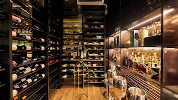 Uma adega com prateleiras cheias de garrafas de vinho, um espaço de bar com garrafas e copos, e uma estante dourada para vinhos.